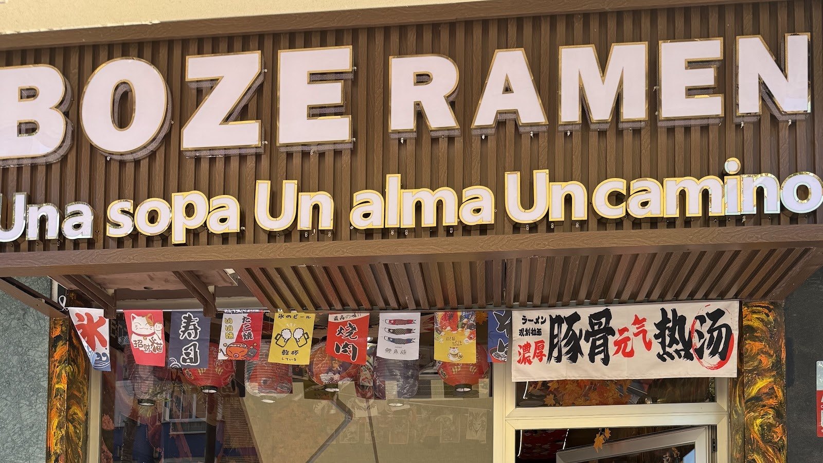 Letrero luminoso BOZE RAMEN con letras blancas sobre fachada de listones de madera